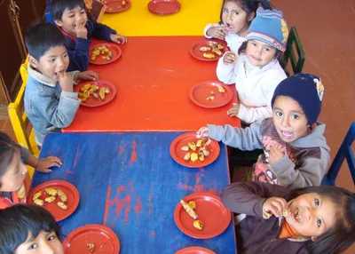 Krippenkinder sitzen an einem langen Tisch beim Essen