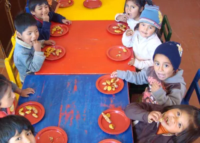 Krippenkinder sitzen an
  einem langen Tisch beim Essen